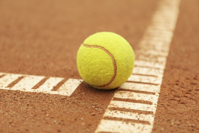 Light green tennis ball on clay court, close up