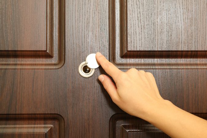 Woman hand hold peephole of wooden door