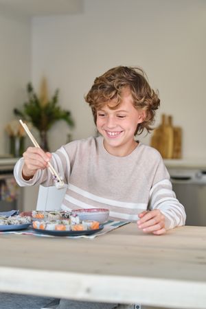 Smiling child having sushi for lunch in kitchen at home