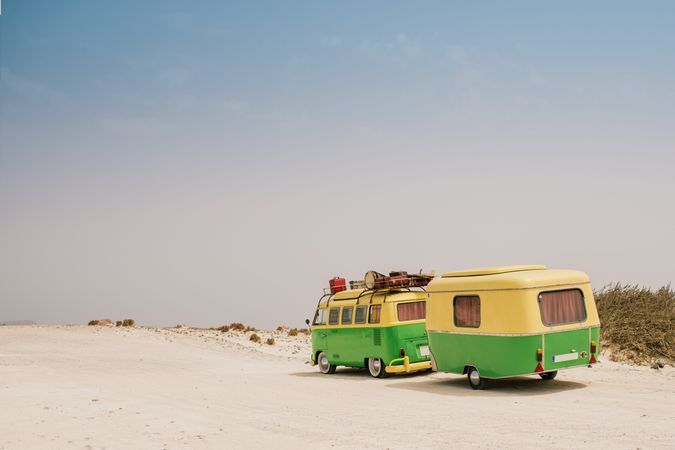Colorful minibus with trailer parked on sandy shore in sunny day