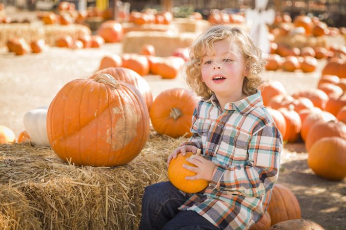 Little Boy Sitting and Holding His Pumpkin Outside