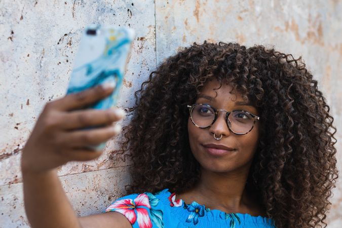 Glad Black woman taking selfie near wall