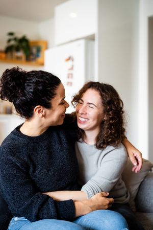 Happy lesbian couple embracing on sofa smiling and looking at each other