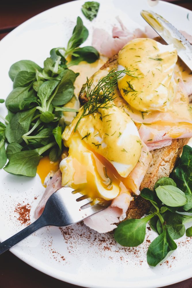 Eggs Benedict with yoke broken with greens, coffee, top view, close up