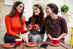 Women friends smiling at something on a friend’s smartphone