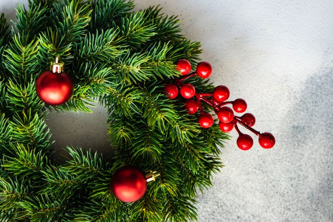 Close up of Christmas wreath with red baubles and holly on marble counter