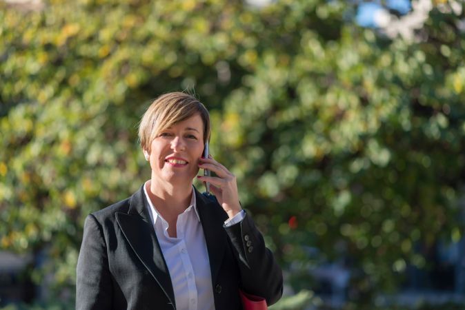 Businesswoman speaking on phone in front of hedge
