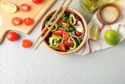 Salad with sesame and kitchen accessories on grey background, top view