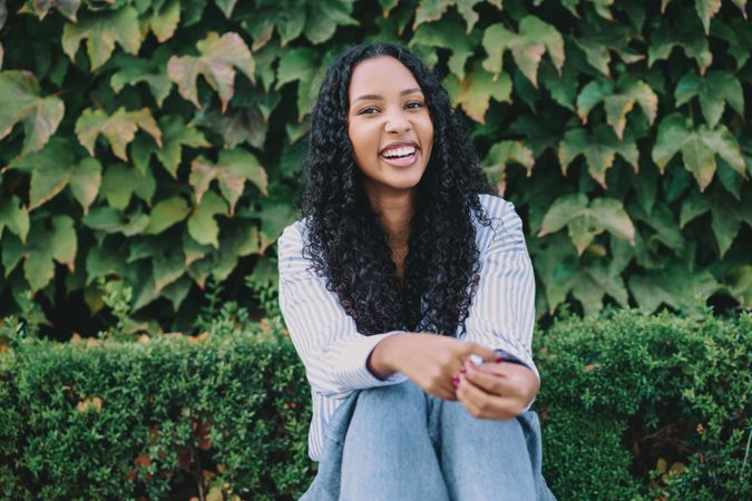 A joyful and smiling young woman is sitting comfortably among lush greenery and nature