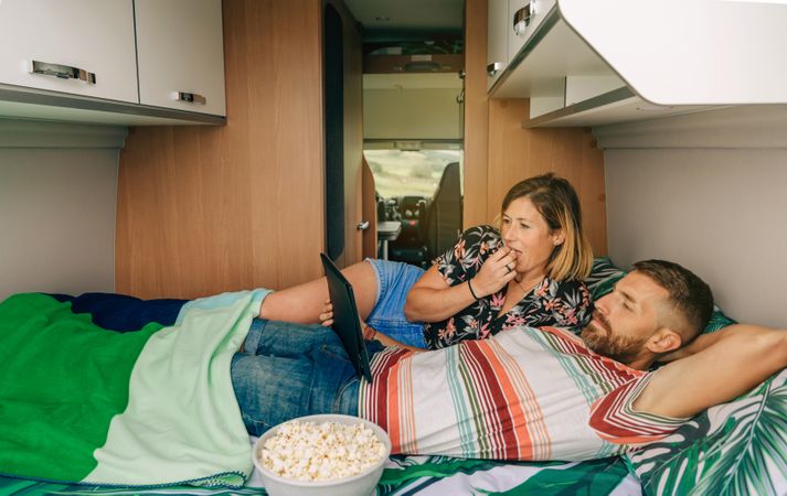 Male and female relaxing on bed in motorhome with popcorn