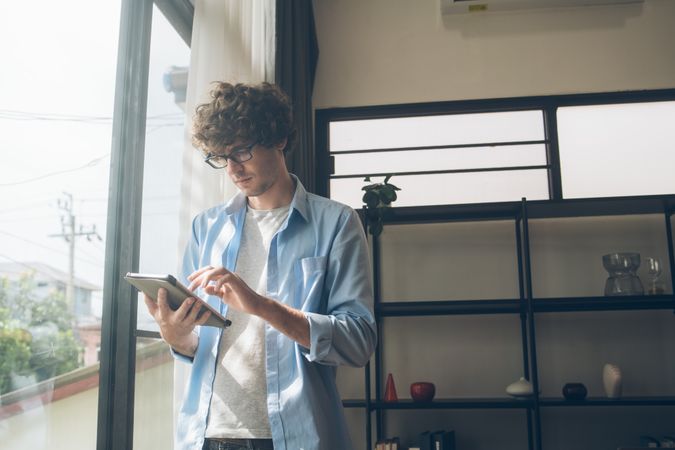 Business man using digital tablet while standing at window working at home