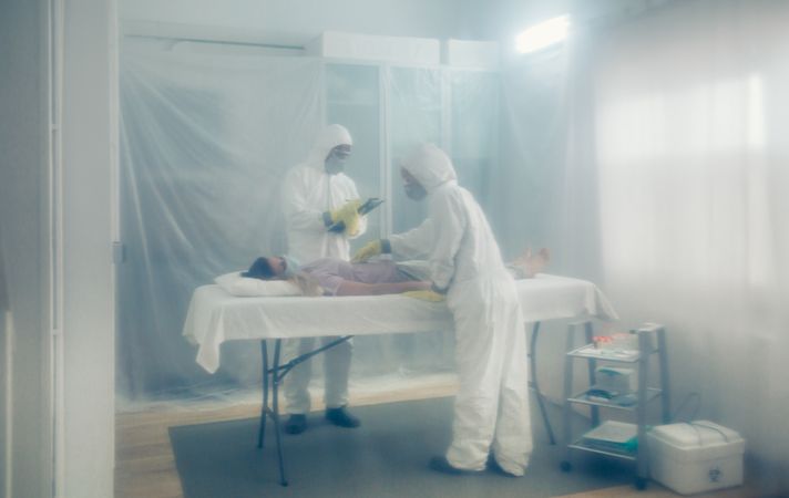 Doctors in bacteriological protection doing medical check to patient lying on a gurney