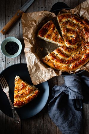 From above crop cook holding hot baking dish with fresh puff pastry and serving piece of borek on plate