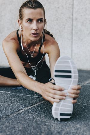 Close up of a woman athlete stretching her leg while listening to music using earphones