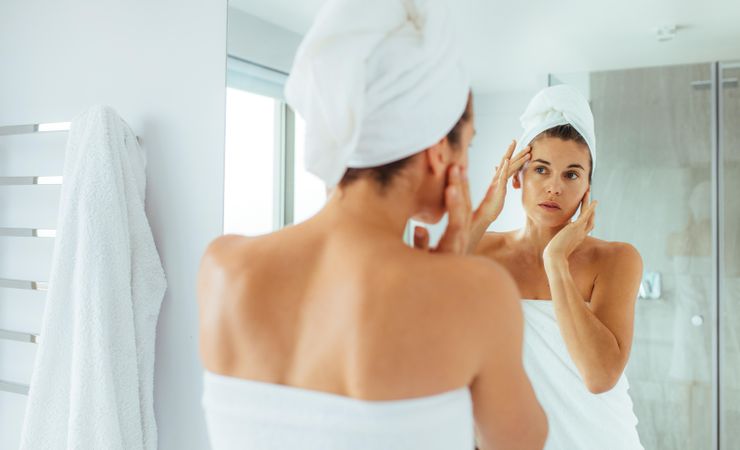 Woman massaging her face looking at a mirror in bathroom