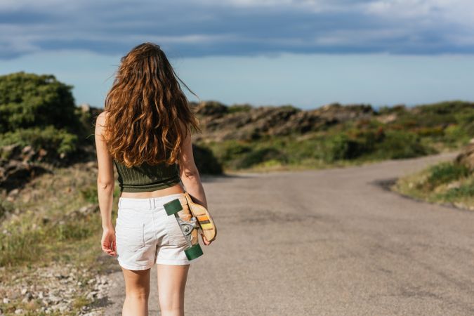 Anonymous skater with longboard walking on pavement against mount