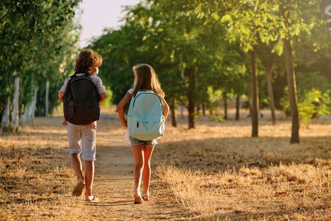 Boy and girl with backpacks walking on path