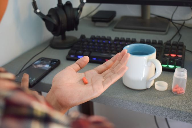 Person sitting at desk with medication in palm of hand