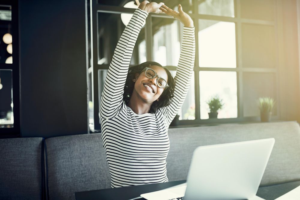 Happy woman sitting with laptop in cafe and stretching