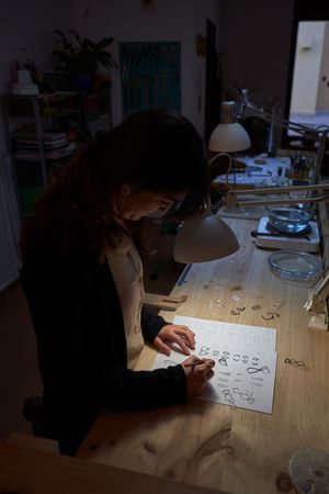 Female master painting jewelry sketches in dark workshop