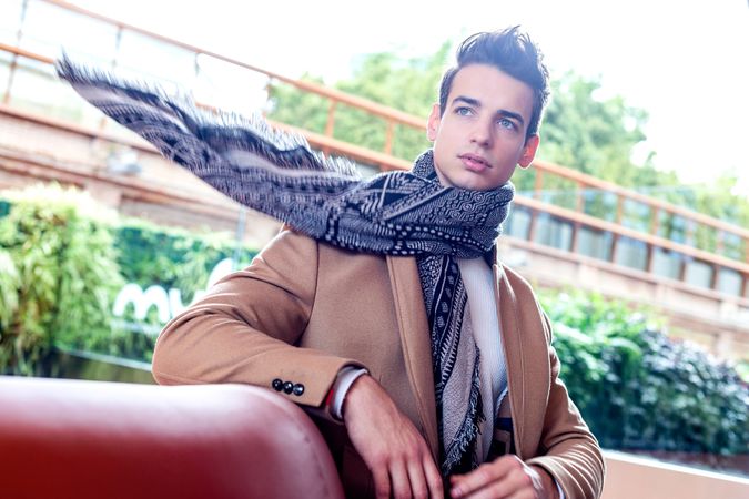 Man in scarf looking around sitting on a leather bench outside