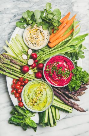 Fresh colorful vegetables and dips with hummus, avocados, asparagus, carrots on marble background