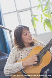 Female singing along while strumming guitar in living room of bright loft 5oa11b
