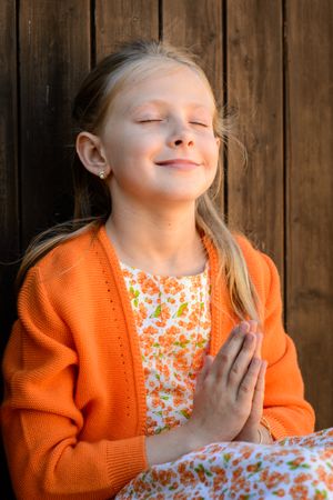 Mindful girl with praying hands against wooden wall