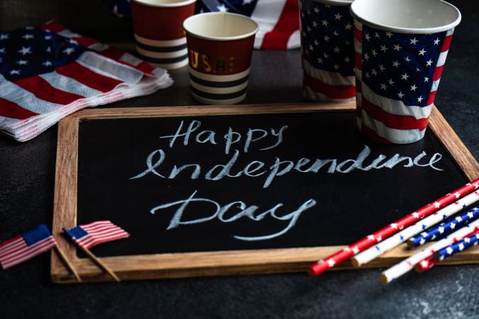 Chalkboard with the words "Happy 4th of July" with American flags and drink straws and cups