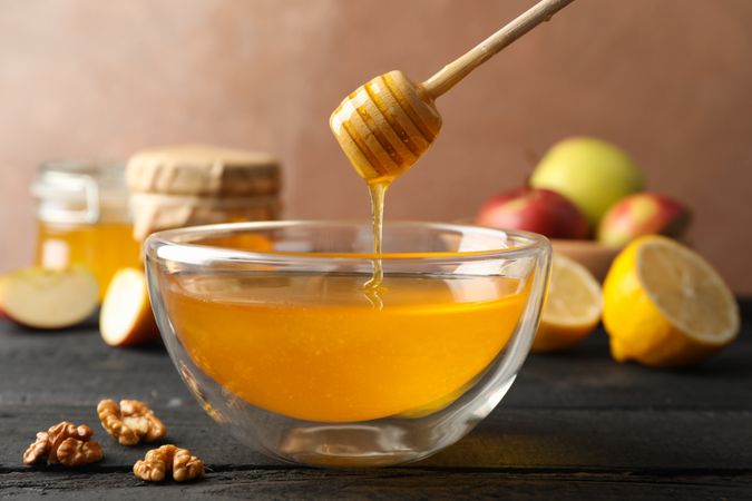 Bowl with honey, dipper and walnut on wooden background, close up