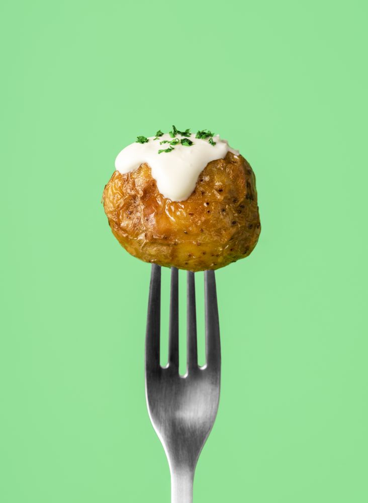 Single roasted potato with sour cream sauce drip on a fork