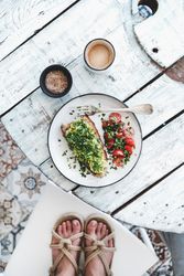 Avocado toast on sourdough bread, cherry tomatoes, coffee, with feet, on light background