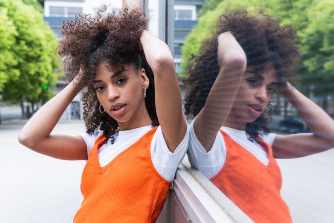 Black woman touching curly hair against glass wall in city