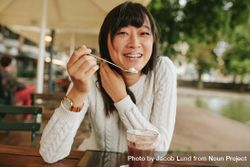 Shot of happy young woman at outdoor cafe eating cold dessert of ice cream 4BvzM4