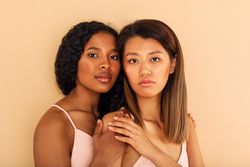 Two female friends standing with hands on each others shoulders in studio shoot