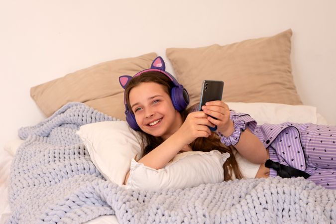 Girl lying in bed with headphones and smartphone