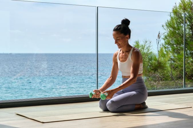 Slim sportswoman training with dumbbells on terrace against sea