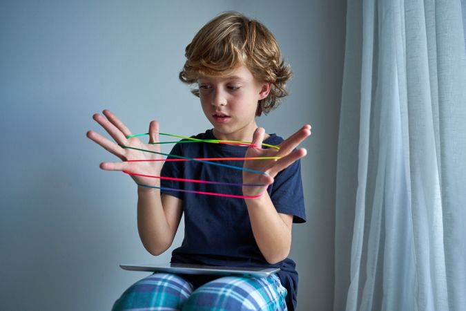 Adorable preteen boy playing cats cradle game