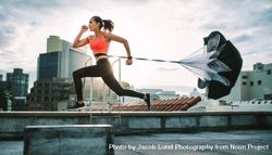 Female athlete training on terrace of a building with a parachute tied behind her bGrmv4