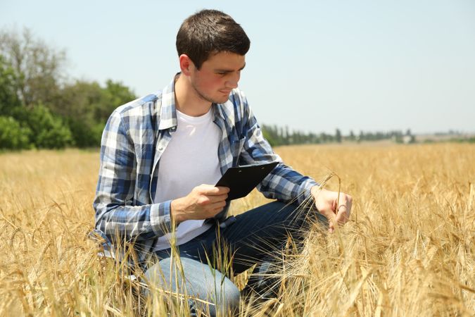 Young man with clipboard in barley field. Agriculture business