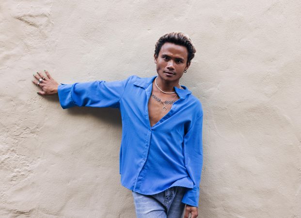 Male in blue shirt and jeans leaning against wall, copy space