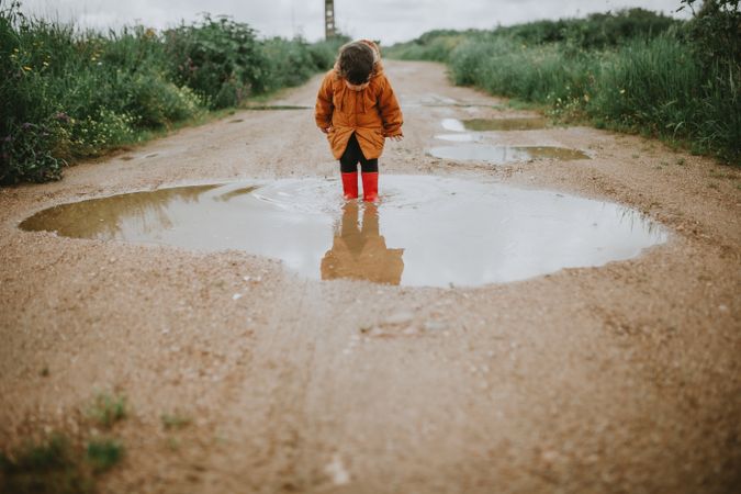 Adorable toddler jumps into a rain puddle
