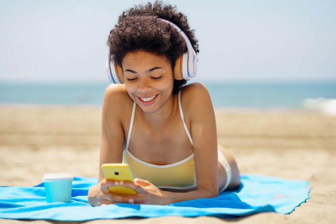 Female with curly hair on beach towel smiling at phone