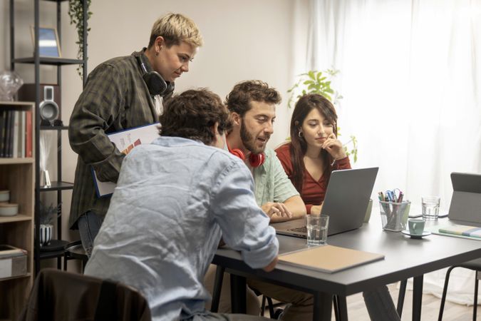 Young diverse creative team discussing project around laptop in bright co-working space