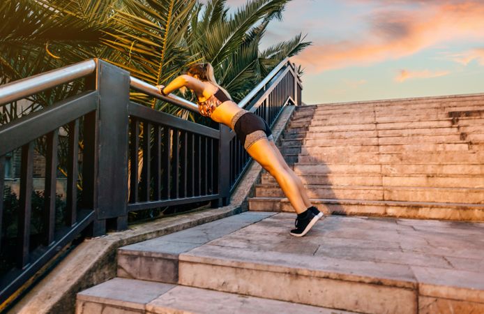 Young blonde woman doing push ups over railing banister at sunset