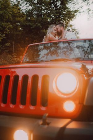 Loving couple sitting on car on road near forest