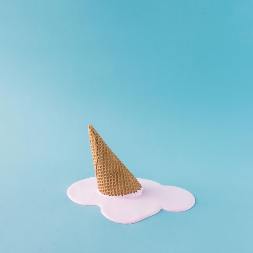 Melted pink ice cream and waffle cone on pastel blue background