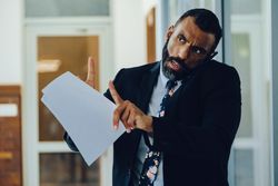 Businessman in suit and tie being interrupted while holding papers and speaking on phone
