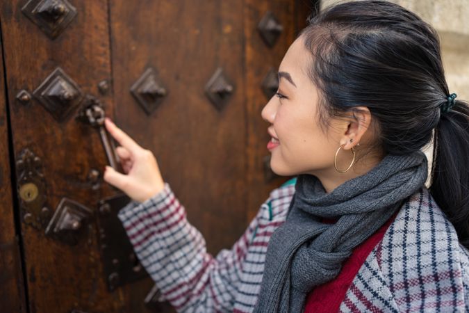 Curious female traveler in casual wear clattering in ancient door at city street