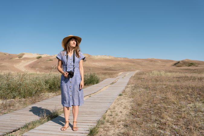 adult woman in straw hat and dress with camera standing on country path